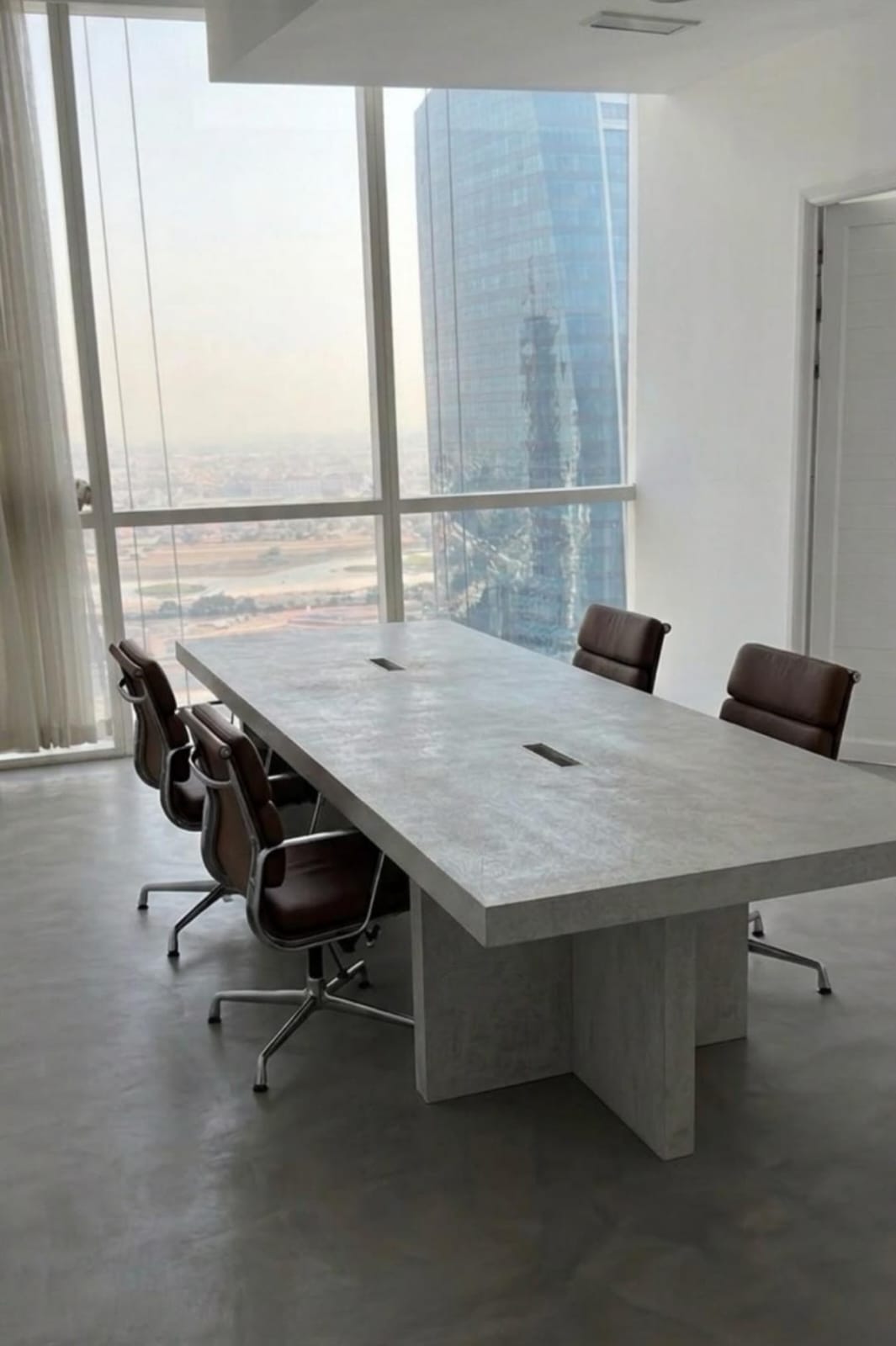 Custom microcement conference table in Dubai high-rise office with cable grommets